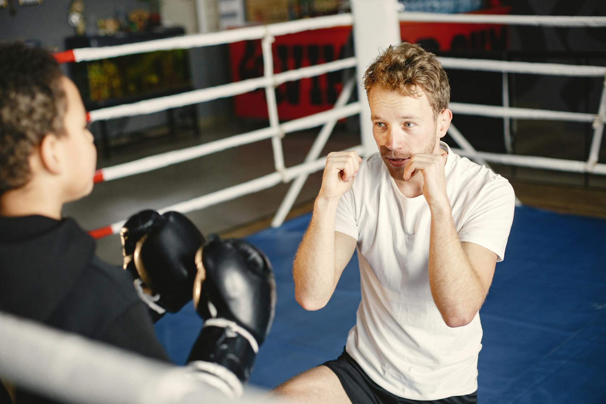 A young athlete practicing boxing drills with a coach inside a boxing ring.
